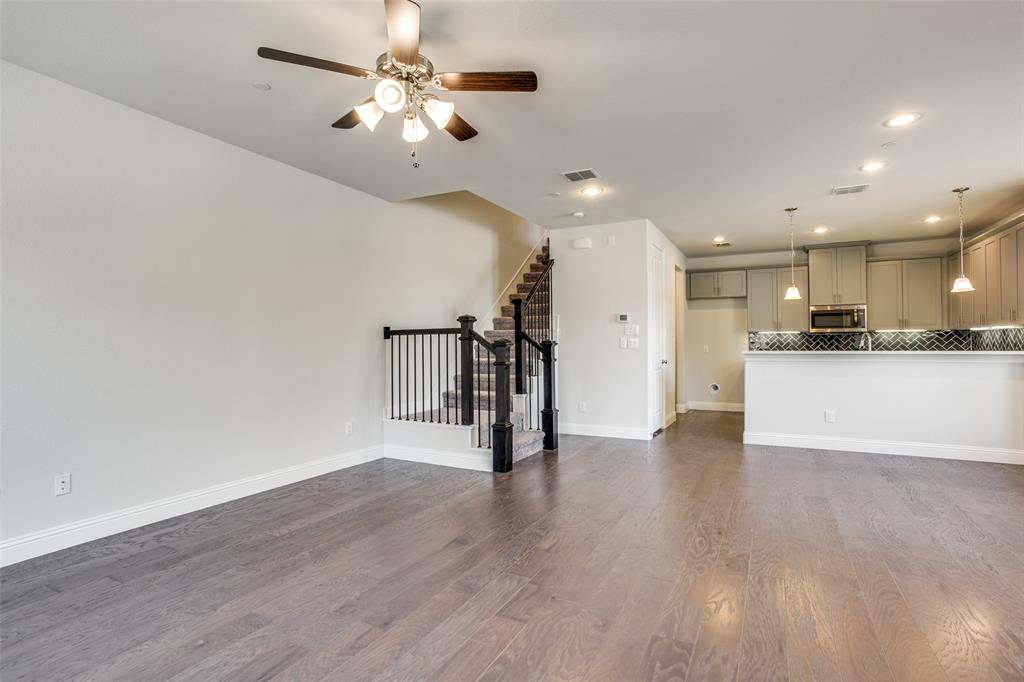 Open-concept interior featuring wood-finish flooring, a kitchen with cabinetry and a breakfast bar, recessed lighting, and a staircase with a black balustrade Open-concept interior featuring wood-finish flooring, a kitchen with cabinetry and a breakfast bar, recessed lighting, and a staircase with a black balustrade