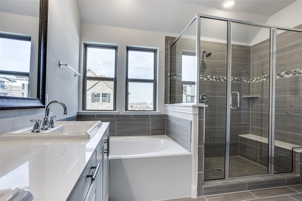 Bathroom featuring a dual-sink vanity with white stone-finish countertop, deep soaking tub, and a walk-in glass-enclosed shower with tiled surround, accent inlay, and built-in bench