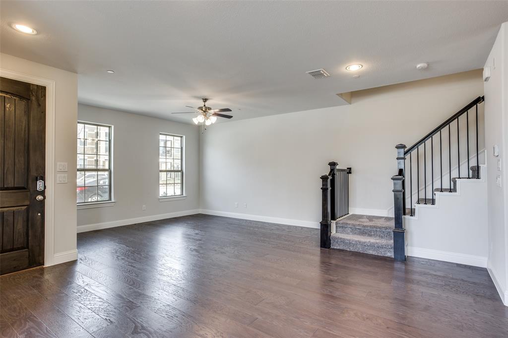 Open-concept interior featuring wood-finish flooring, recessed lighting, a ceiling fan, a dark-stained wood entry door, and a staircase with a black metal railing Open-concept interior featuring wood-finish flooring, recessed lighting, a ceiling fan, a dark-stained wood entry door, and a staircase with a black metal railing