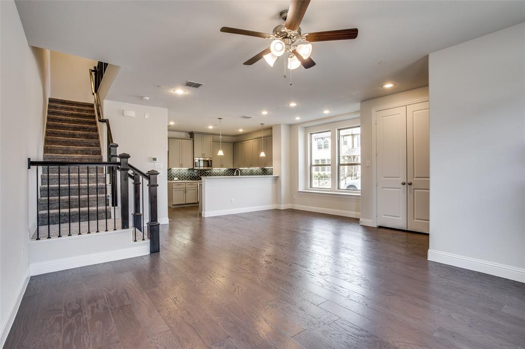Open-concept interior featuring wood-finish flooring, recessed lighting, a ceiling fan, a staircase with decorative metal balusters, and a kitchen with neutral cabinetry Open-concept interior featuring wood-finish flooring, recessed lighting, a ceiling fan, a staircase with decorative metal balusters, and a kitchen with neutral cabinetry