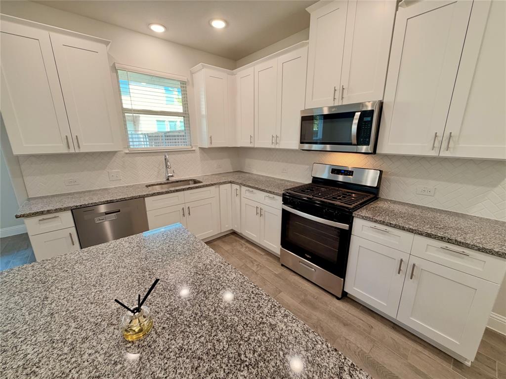 Kitchen featuring white cabinetry, stone-finish countertops, stainless steel appliances, a herringbone-patterned backsplash, and wood-finish flooring Kitchen featuring white cabinetry, stone-finish countertops, stainless steel appliances, a herringbone-patterned backsplash, and wood-finish flooring
