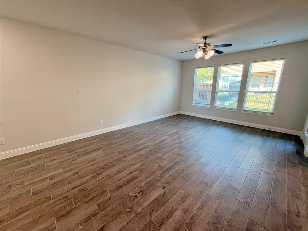 Interior space featuring wood-finish tile flooring, three large windows, and a multi-blade ceiling fan with integrated lighting Interior space featuring wood-finish tile flooring, three large windows, and a multi-blade ceiling fan with integrated lighting