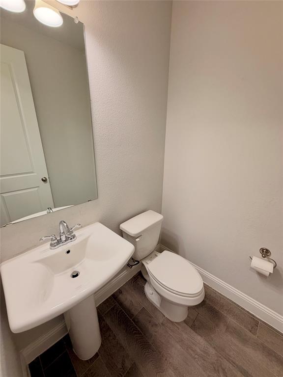 Pedestal sink with a polished chrome faucet, rectangular wall-mounted mirror, three-light vanity fixture, and wood-finish flooring