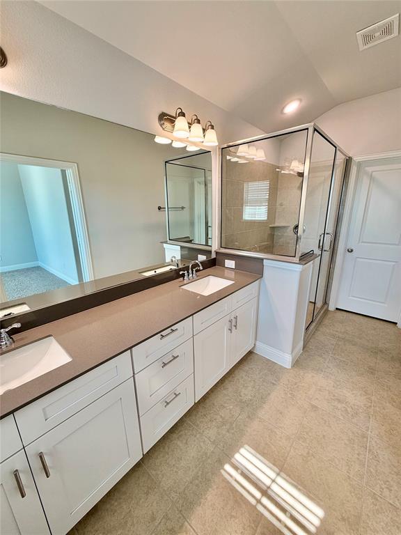 Dual-sink vanity with a solid-surface countertop, white shaker-style cabinetry, a glass-enclosed shower with tile surround, and tile flooring