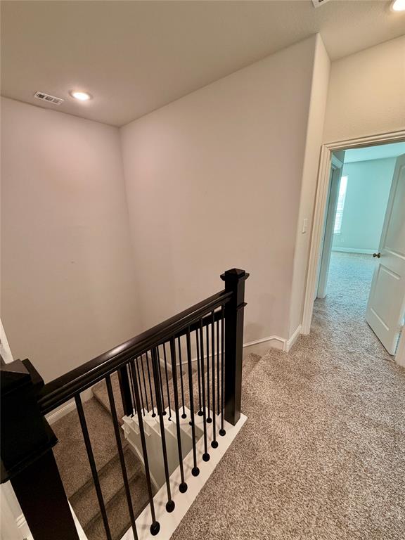 Staircase featuring dark-finished wooden handrails and balusters with carpeted steps, neutral wall tones, and recessed ceiling lighting Staircase featuring dark-finished wooden handrails and balusters with carpeted steps, neutral wall tones, and recessed ceiling lighting
