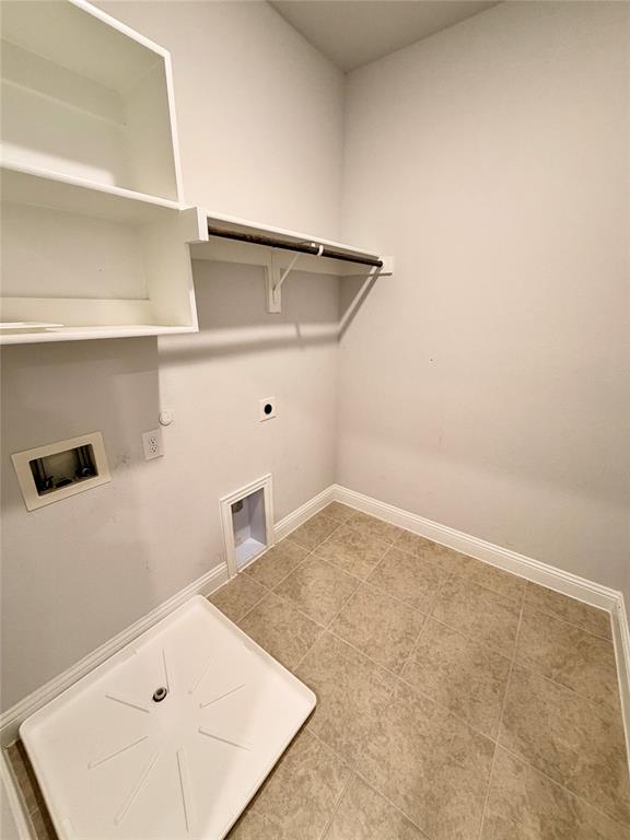 Utility area featuring ceramic tile flooring, built-in shelving, an integrated hanging rod, and a recessed plumbing connection box with a drain pan Utility area featuring ceramic tile flooring, built-in shelving, an integrated hanging rod, and a recessed plumbing connection box with a drain pan