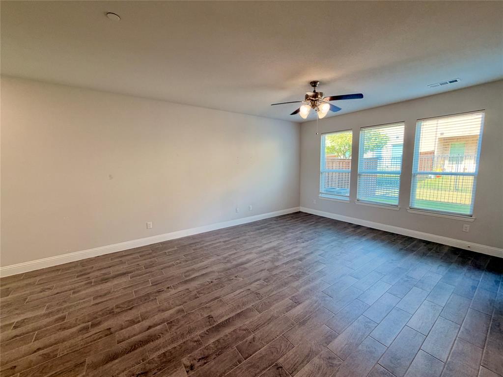 Spacious room featuring wood-finish flooring, neutral wall paint, three large windows, and a ceiling fan with integrated lighting