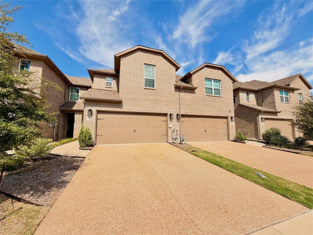 Multi-story brick exterior featuring a multi-gabled roofline, dual-car garages, and an aggregate concrete driveway Multi-story brick exterior featuring a multi-gabled roofline, dual-car garages, and an aggregate concrete driveway