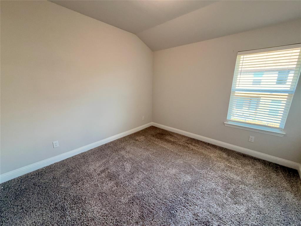 Room featuring neutral wall paint, vaulted ceiling, carpeting, and a single window with installed blinds Room featuring neutral wall paint, vaulted ceiling, carpeting, and a single window with installed blinds