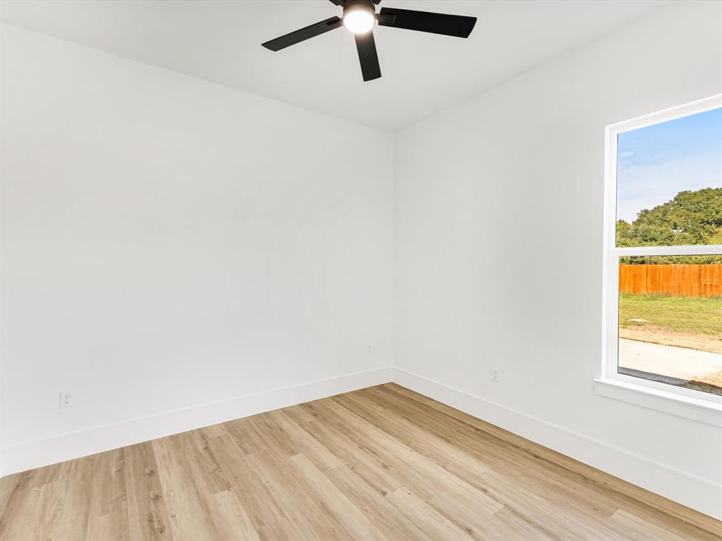 Bright interior space featuring wood-finish flooring, crisp white walls, a multi-blade ceiling fan, and a window with exterior landscape exposure