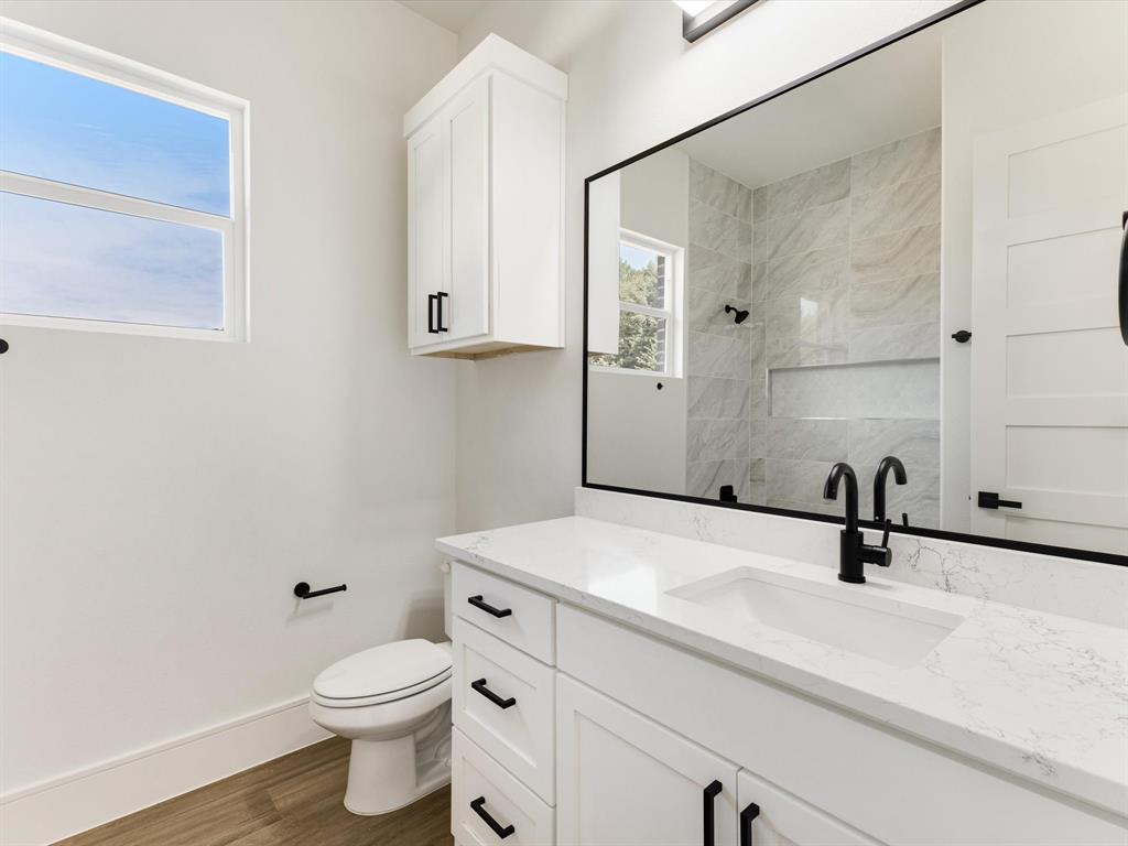 Bathroom vanity featuring a stone-surface countertop, integrated undermount sink, matte black hardware, and wood-finish flooring