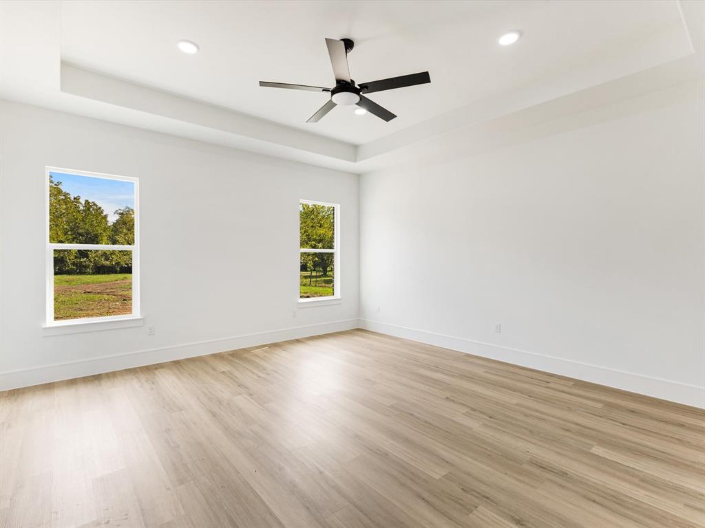 Tray ceiling featuring a central matte black ceiling fan, recessed lighting, wood-finish flooring, and windows with natural light
