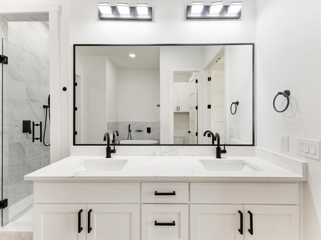Dual-sink vanity with white cabinetry, stone-finish countertop, matte black hardware, integrated rectangular basins, and a large rectangular mirror framed in black