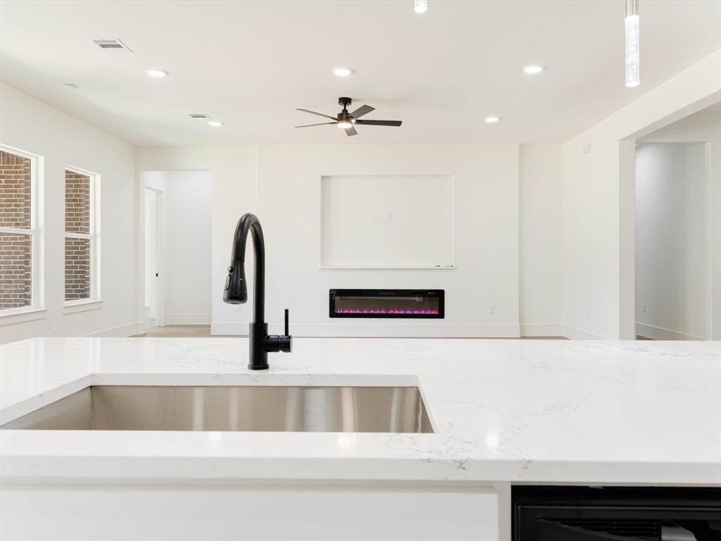 Kitchen featuring a large solid-surface island with an undermount stainless steel sink and a matte black pull-down faucet, complemented by a recessed wall-mounted fireplace and recessed ceiling lighting