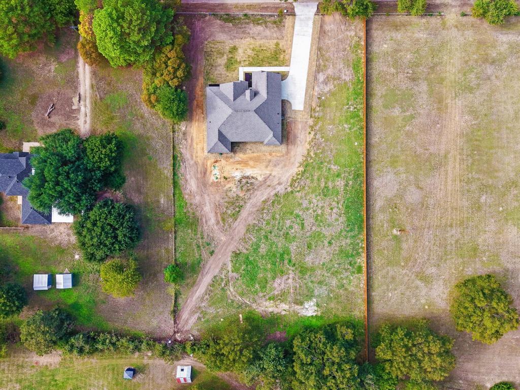 Aerial view of a residential property featuring a hipped roof structure, a paved concrete driveway, and expansive acreage enclosed by perimeter fencing