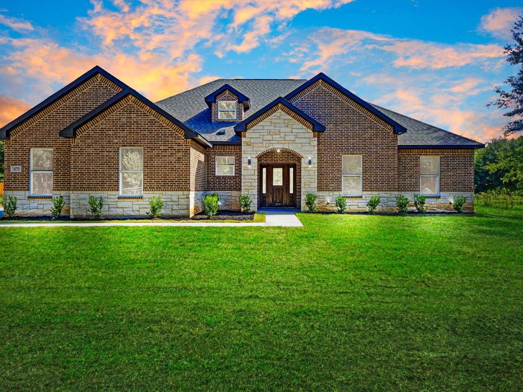 Exterior facade featuring a combination of red brick and light-toned stone masonry, a covered entryway with an arched stone surround, a multi-gabled roofline, and a manicured front lawn