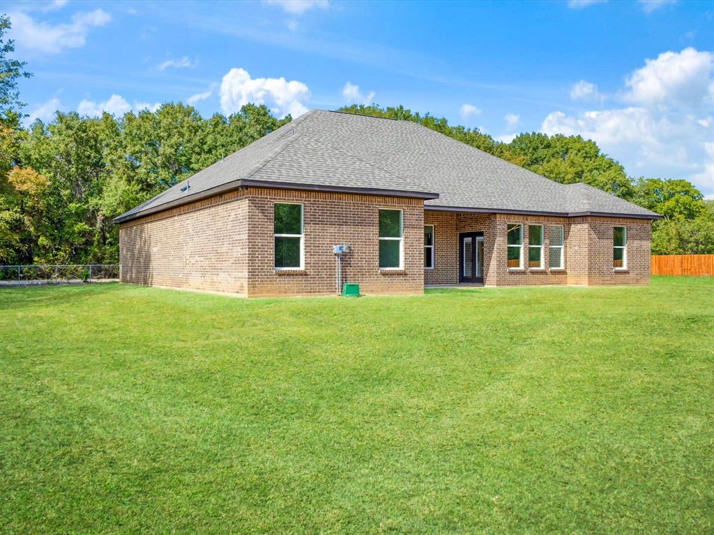 Single-story brick exterior featuring a hipped roof, multi-pane windows, and a sprawling grass yard with perimeter tree growth