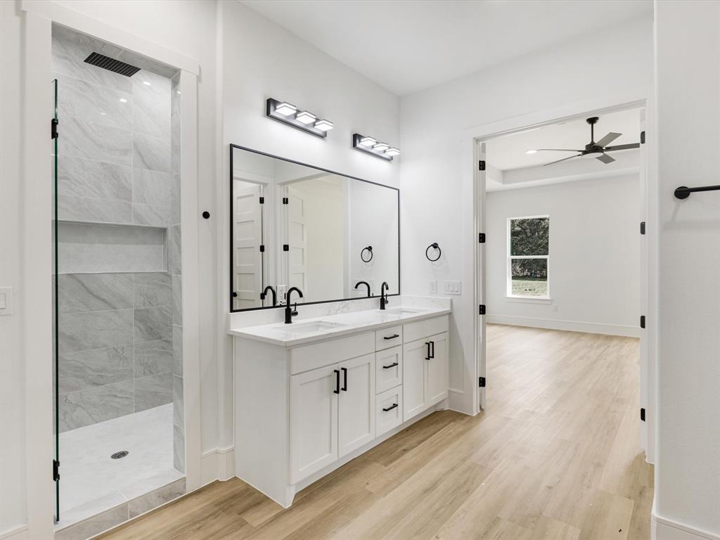 Double vanity featuring white cabinetry, quartz countertops, matte black fixtures, a full-width mirror, and a walk-in shower with floor-to-ceiling tile surround and recessed shelving