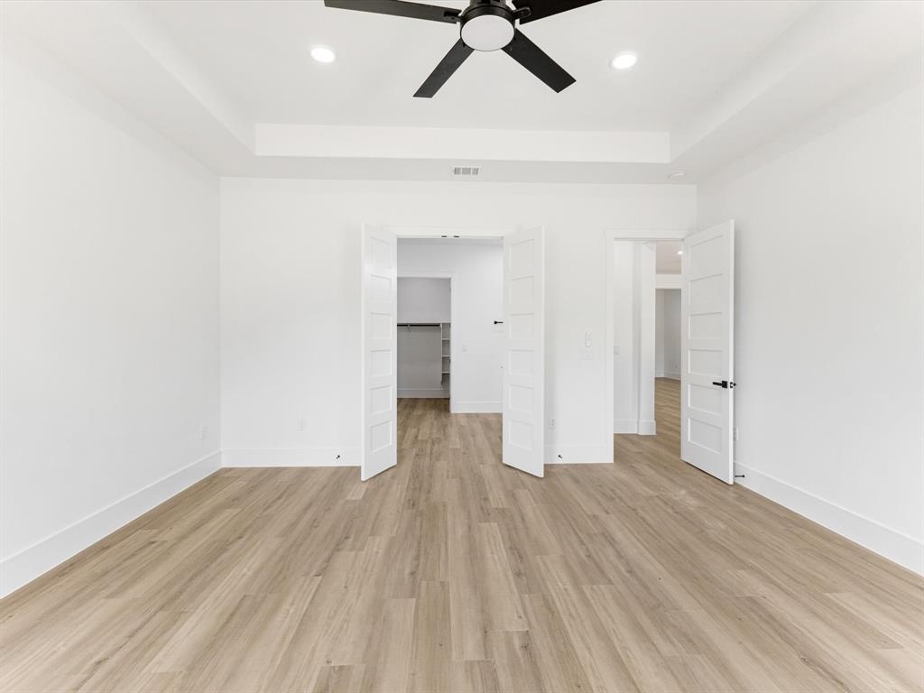Tray ceiling with recessed lighting, matte black ceiling fan, wood-finish flooring, and white paneled interior doors