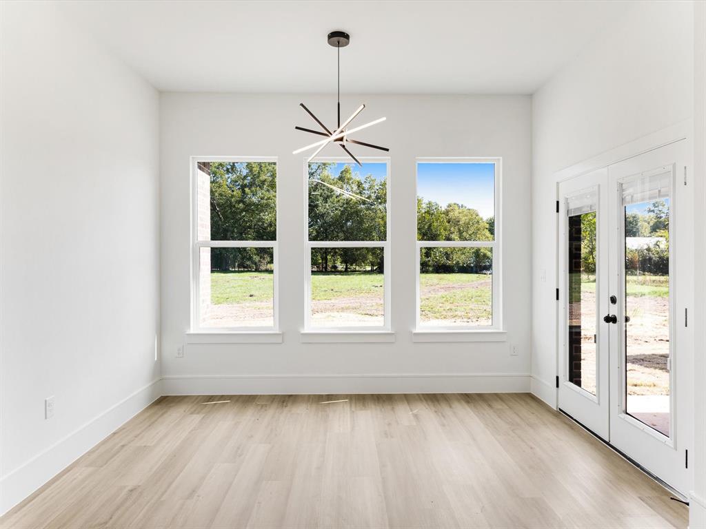 Modern space featuring light-toned wood-finish flooring, three vertical windows, a contemporary multi-spoke pendant light fixture, and glass-paneled double doors
