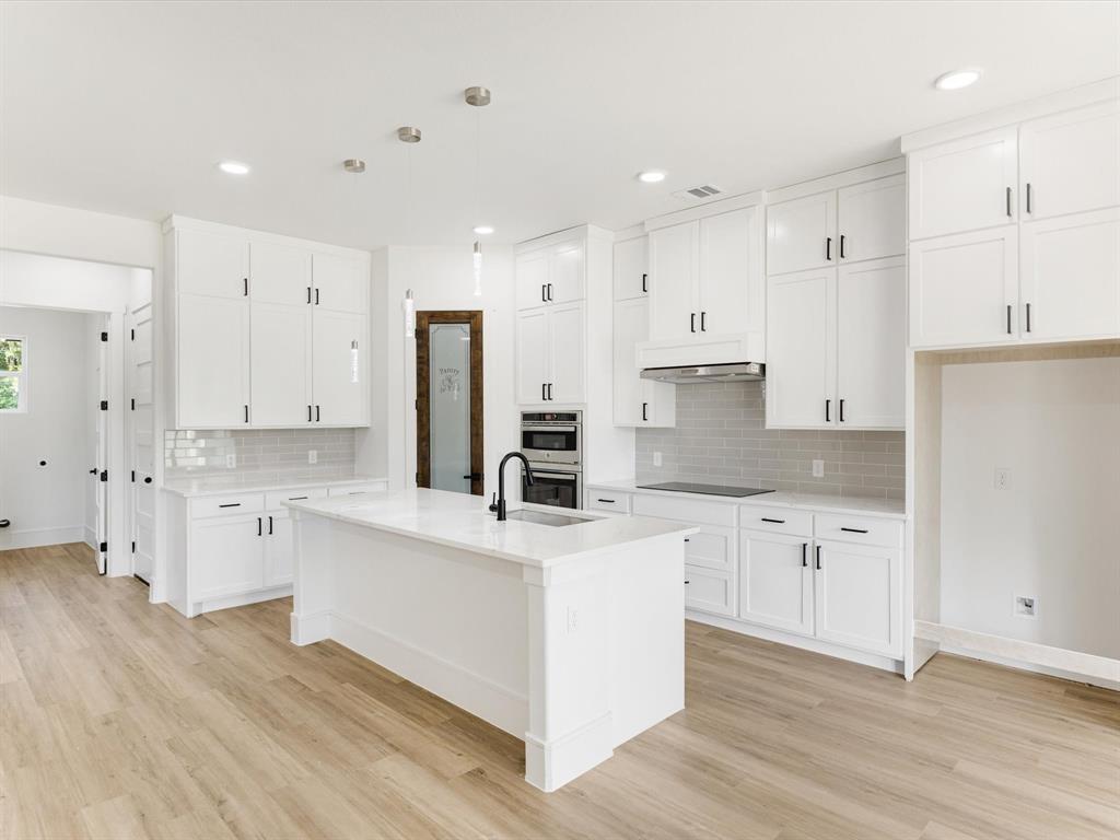 Kitchen featuring white Shaker-style cabinetry, a central island with a matte black faucet, subway tile backsplash, wood-finish flooring, and built-in stainless steel appliances