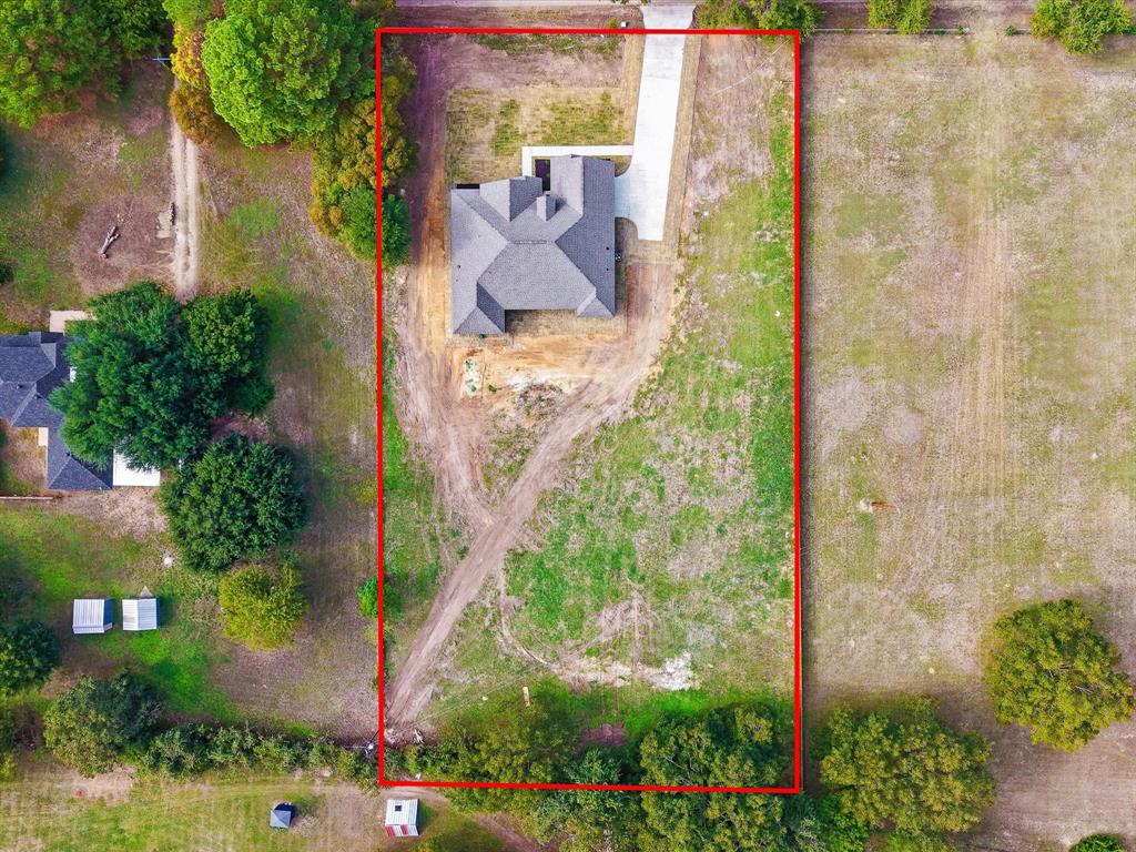 Aerial view of a rectangular property featuring a single-story structure with a multi-gable roof, concrete driveway, and expansive undeveloped land