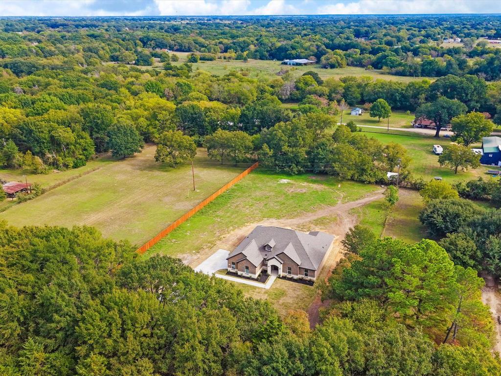 Aerial perspective of a multi-gabled residence featuring brick and masonry exterior finishes, surrounded by expansive acreage, mature tree clusters, and a wooden privacy fence