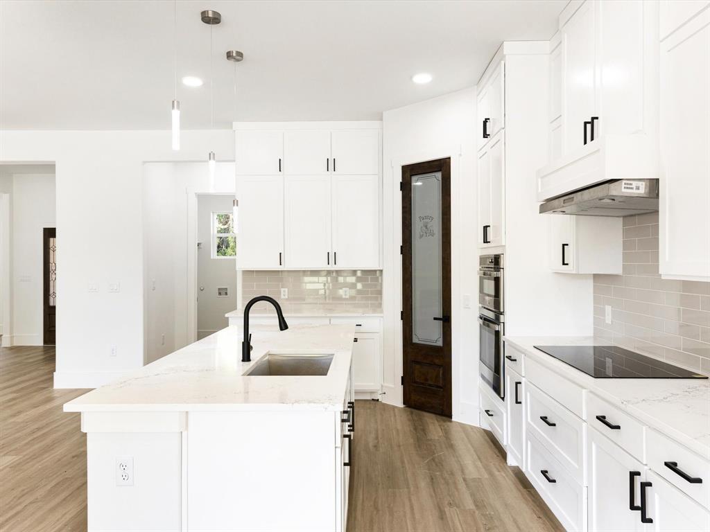 Kitchen featuring white cabinetry, quartz countertops, a central island with a matte black faucet, integrated stainless steel double wall ovens, and wood-finish flooring