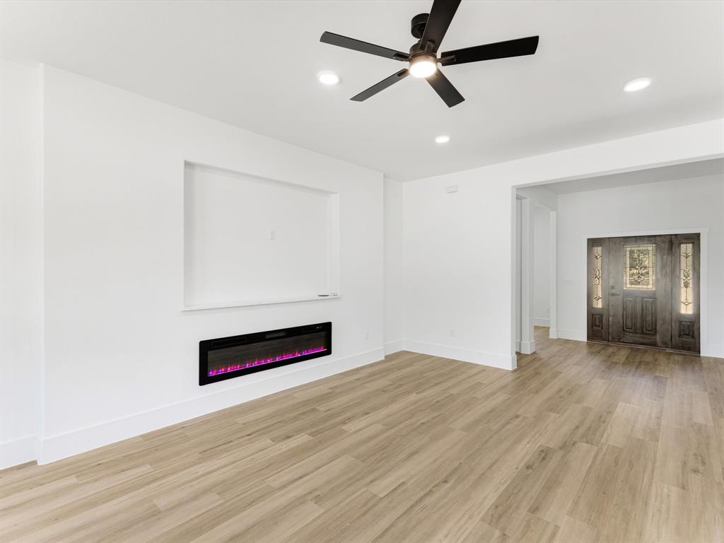 Interior space featuring wood-finish flooring, a wall-mounted electric fireplace, recessed lighting, a ceiling fan with integrated lighting, and a front entry door with glass panel detailing
