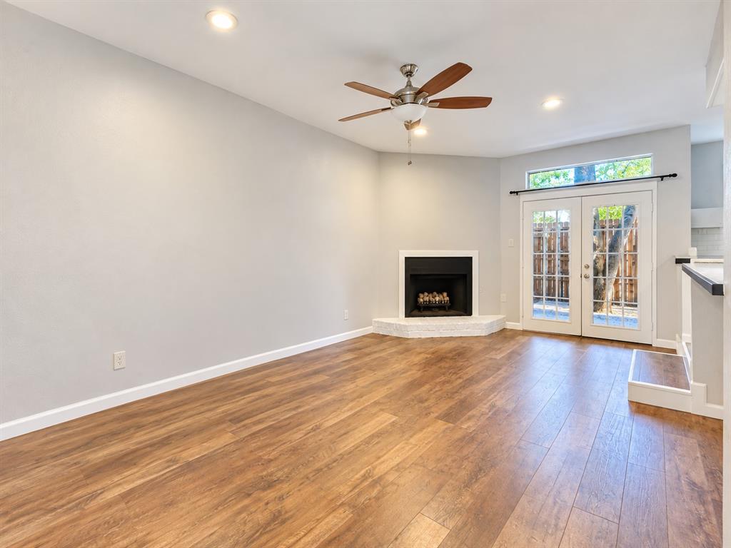 Living area featuring wood-finish flooring, a corner fireplace with a raised hearth, recessed lighting, a ceiling fan, and glass-paned double doors