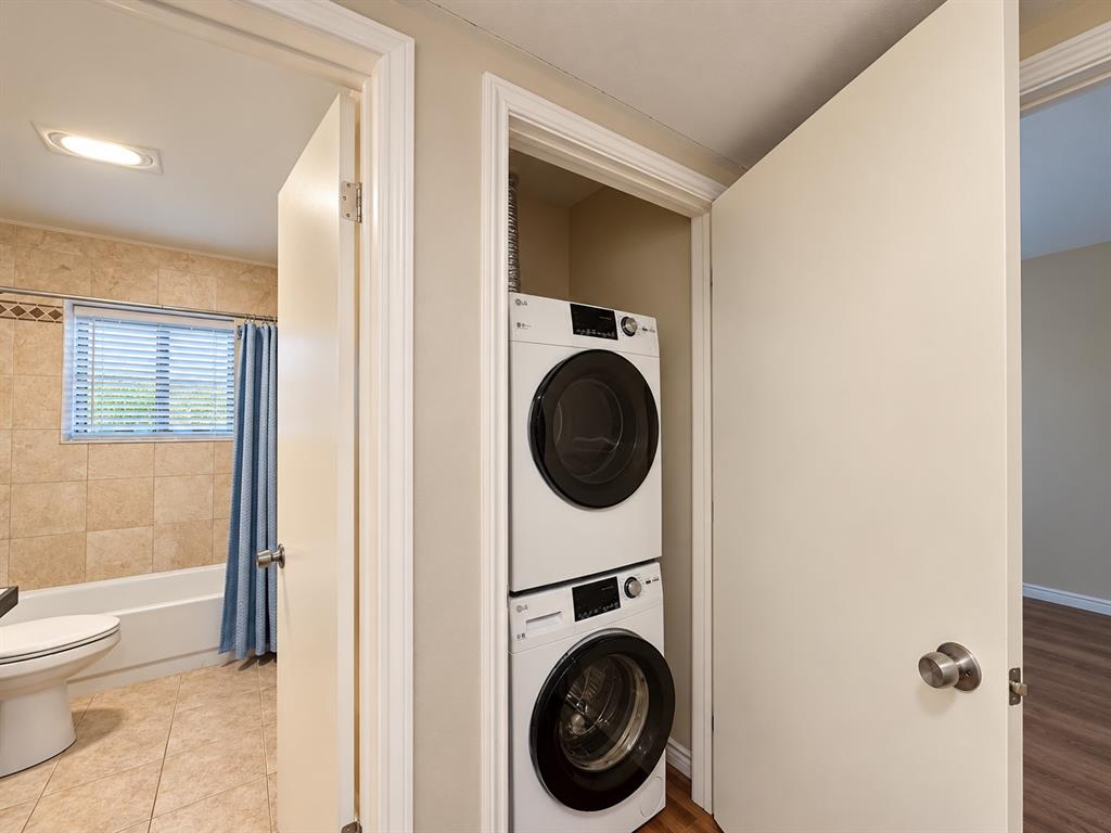 Dedicated laundry closet featuring a stackable washer and dryer unit, set beside a bathroom finished with neutral wall tiling and floor tiling