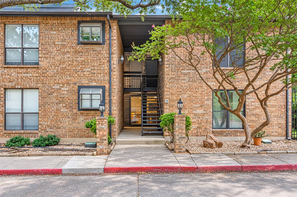 Multi-story brick exterior featuring a recessed entrance, black metal staircase, multi-pane windows, and exterior light fixtures