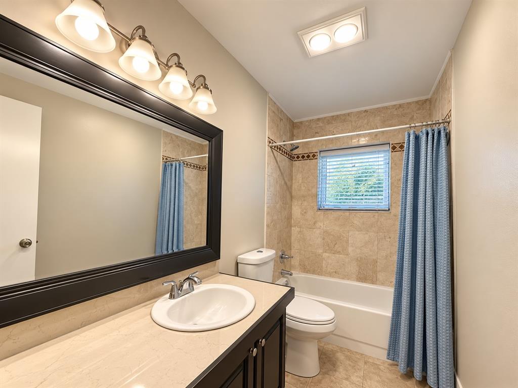 Bathroom featuring dark wood-finish cabinetry, a neutral countertop with an integrated basin, a large framed vanity mirror, and stone-tile tub surround with decorative inlay