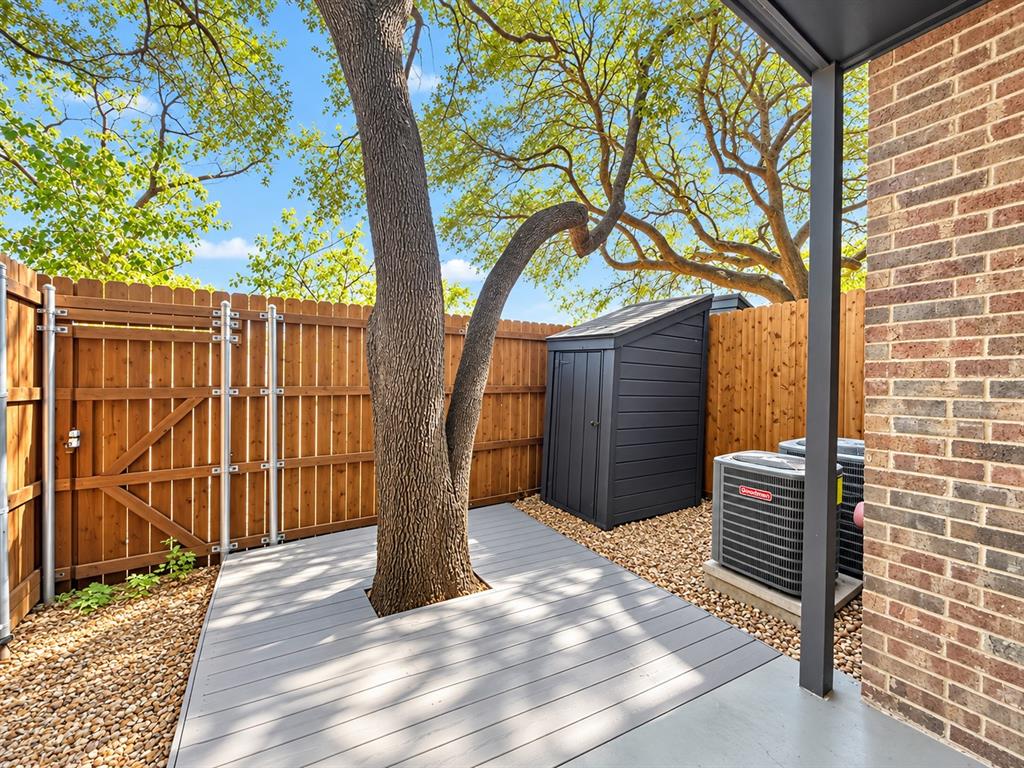 Exterior space featuring a grey composite deck, wood privacy fencing, a gravel landscape, and a brick facade