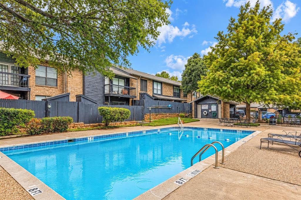 Outdoor swimming pool featuring a concrete deck, metal handrails, and surrounding landscaping with mature trees