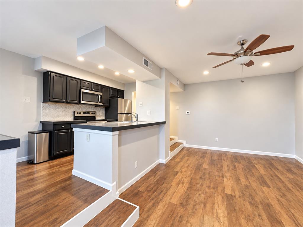 Kitchen featuring dark cabinetry, solid-surface countertops, light-toned backsplash tile, wood-finish flooring, and a ceiling-mounted fan with integrated lighting