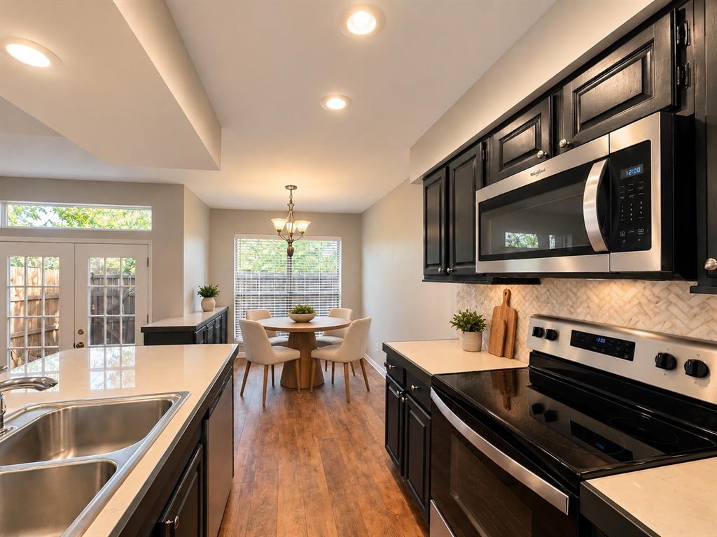 Kitchen featuring dark cabinetry, stainless steel appliances, herringbone-patterned backsplash, light-toned countertops, and wood-finish flooring