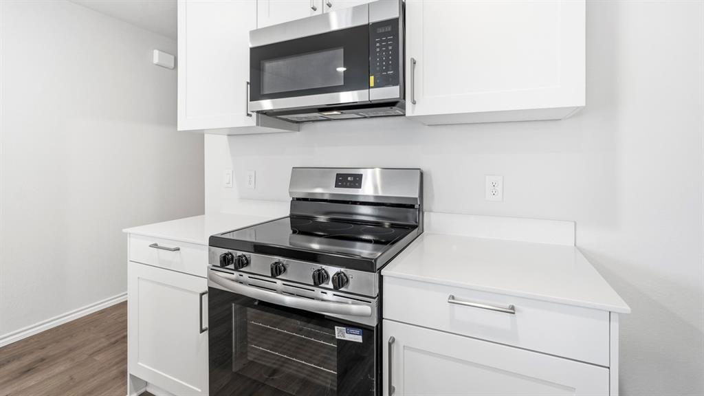White cabinetry, stainless steel range, stainless steel microwave, white countertops, and wood-finish flooring