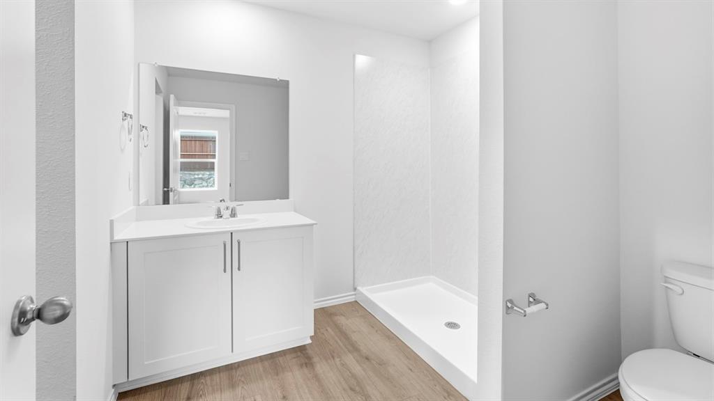 White vanity with integrated sink, rectangular mirror, wood-finish flooring, and a stand-up shower