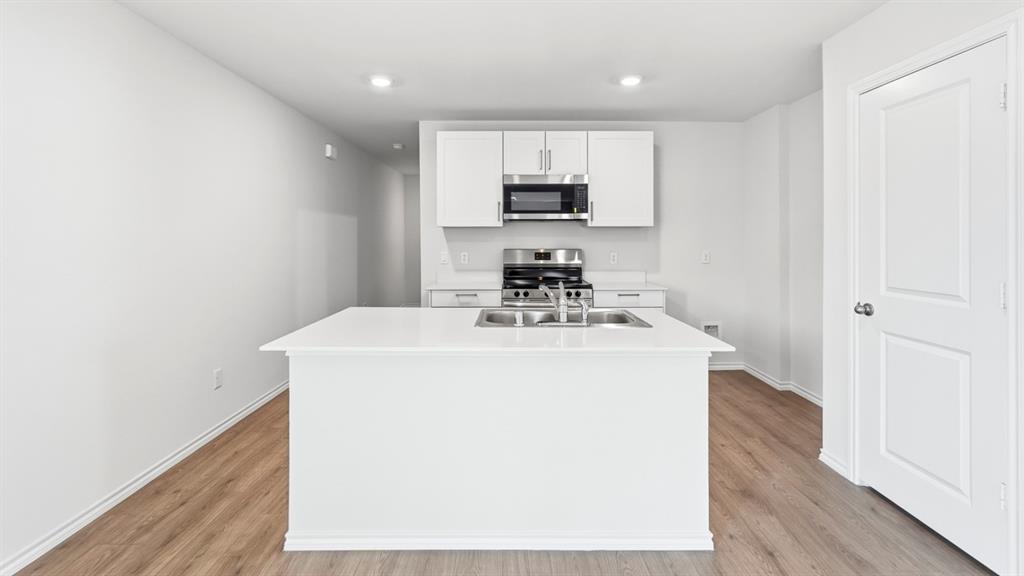 Kitchen featuring a central island with an undermount sink, white cabinetry with stainless steel hardware, stainless steel appliances, and wood-finish flooring