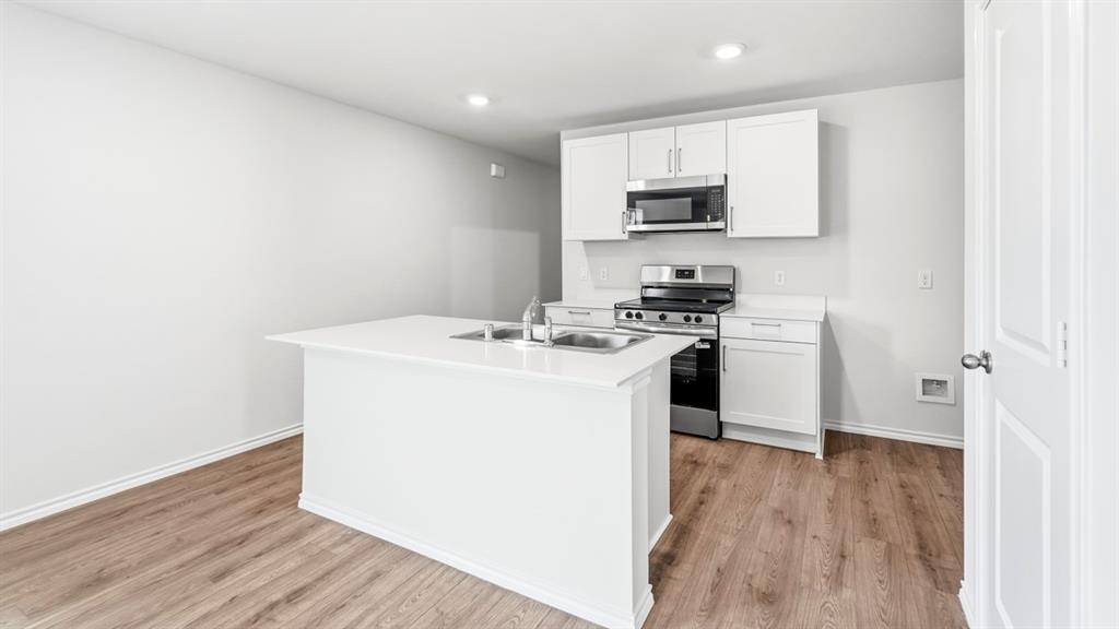 Kitchen featuring white shaker cabinetry, stainless steel appliances, a center island with an undermount double basin sink, and wood-finish flooring