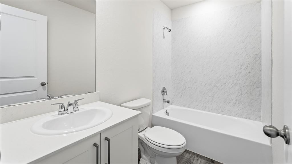Bathroom featuring a single vanity with an integrated sink, polished chrome faucet, and a spacious bathtub with a textured surround