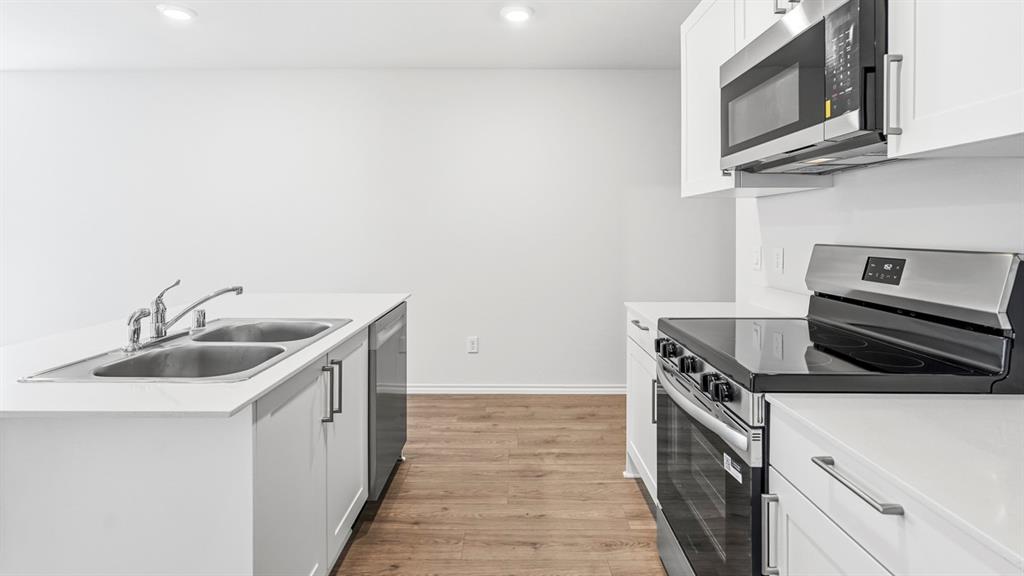 Modern kitchen featuring white cabinetry, light countertops, wood-finish flooring, stainless steel appliances, and a double basin sink