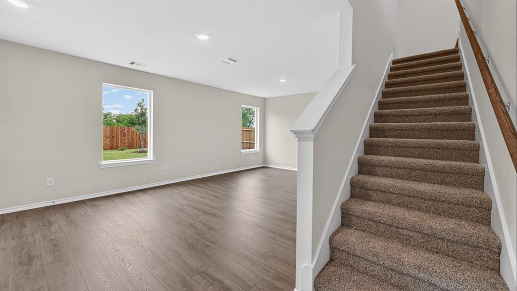 Spacious room featuring wood-finish flooring, two windows, recessed lighting, and a carpeted staircase with a wood handrail