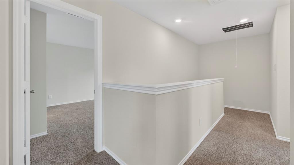 Carpeted upper-level landing featuring a white railing, recessed lighting, and access to additional rooms