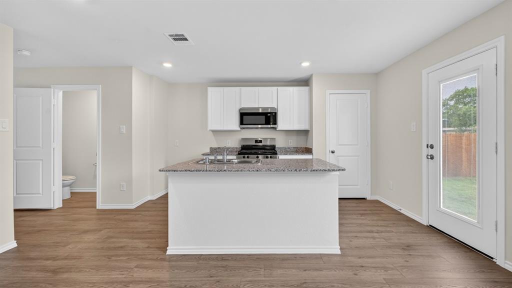 Open-concept kitchen featuring an island with a granite countertop, white cabinetry, stainless steel appliances, wood-finish flooring, and a glass-paneled exterior door