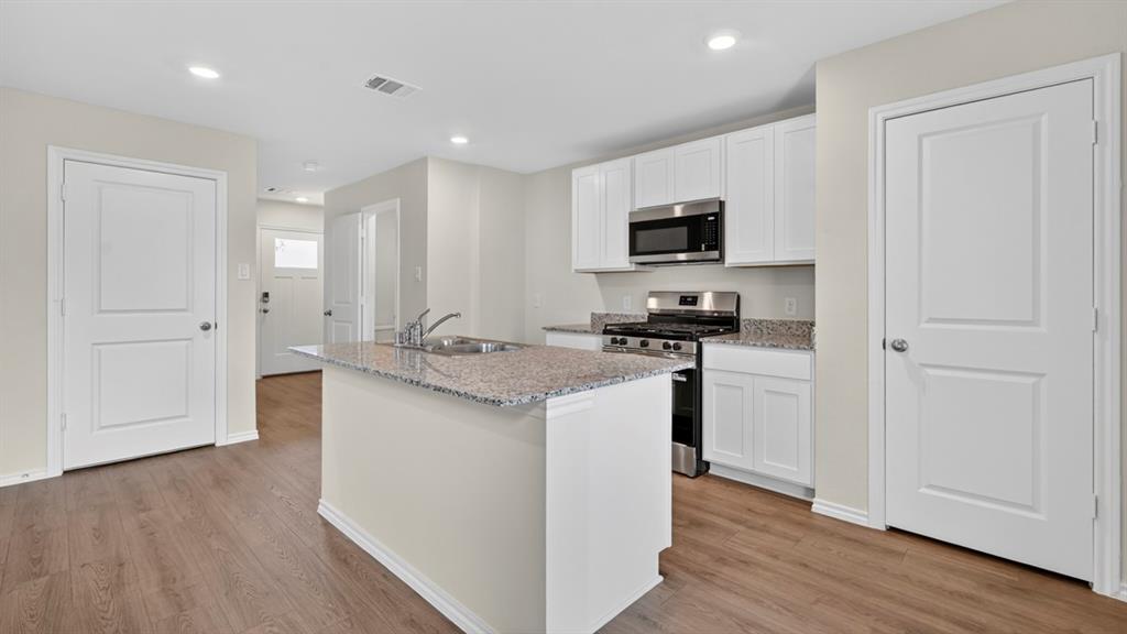 Kitchen featuring a granite-topped island with an undermount sink, stainless steel appliances, white cabinetry, and wood-finish flooring