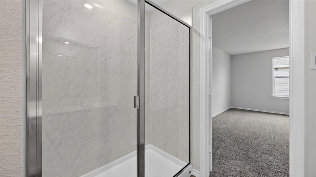 Walk-in shower with clear glass enclosure and light-toned, textured wall panels