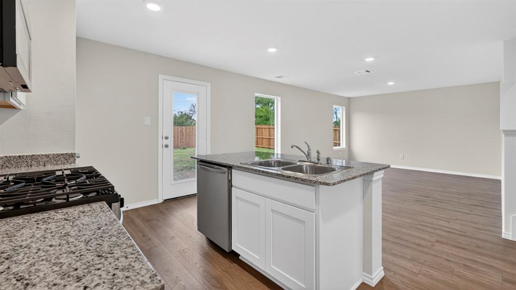 Kitchen island featuring a double basin stainless steel sink with a chrome faucet, granite countertops, and white cabinetry