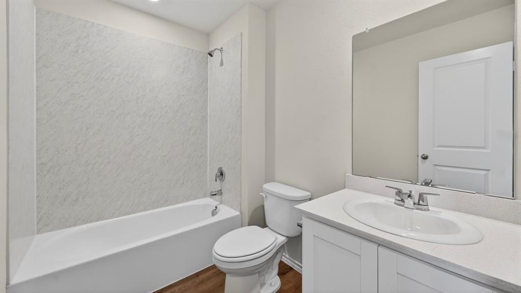 Bathroom featuring a white bathtub with a textured shower surround, chrome fixtures, a white vanity with an integrated sink, a large wall-mounted mirror, and wood-finish flooring
